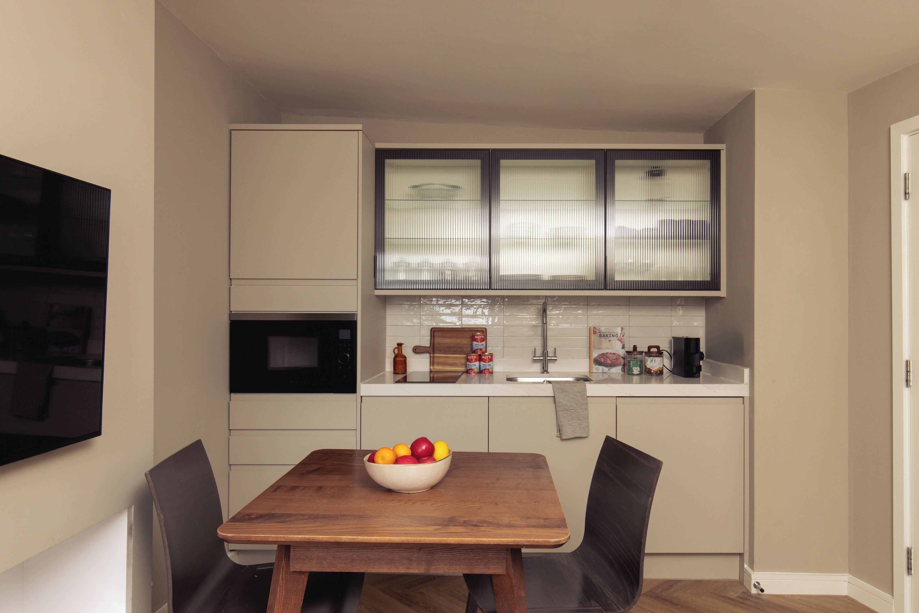 A compact kitchen with a dining table, chairs, and a bowl of fruit.