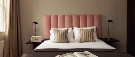 A neatly made bed with a pink headboard, two bedside tables with lamps, and a book on the bed.
