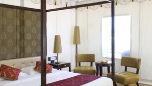 Una cama con dosel con un plaid rojo, suelo de madera y una alfombra estampada.