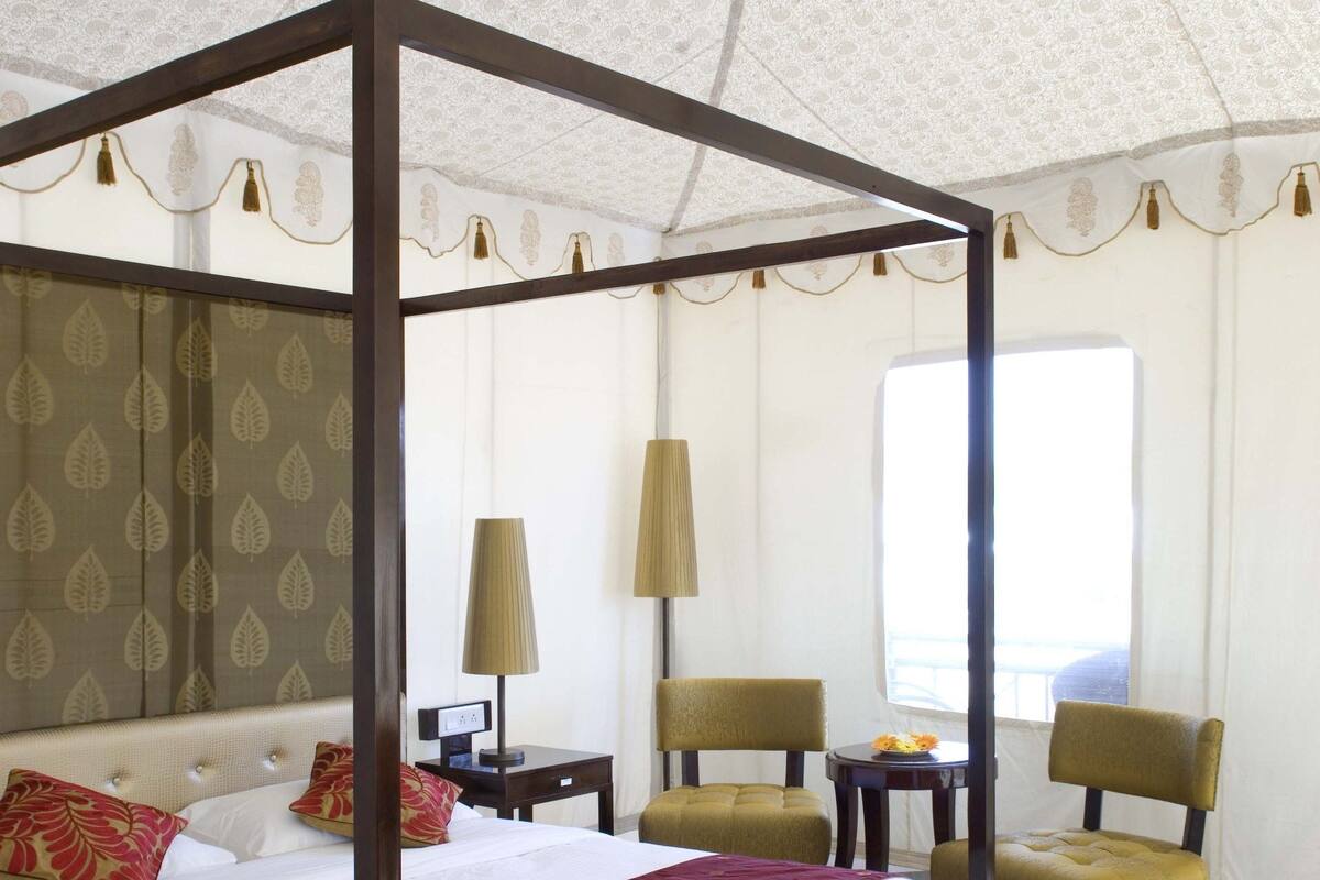 Una cama con dosel con un plaid rojo, suelo de madera y una alfombra estampada.