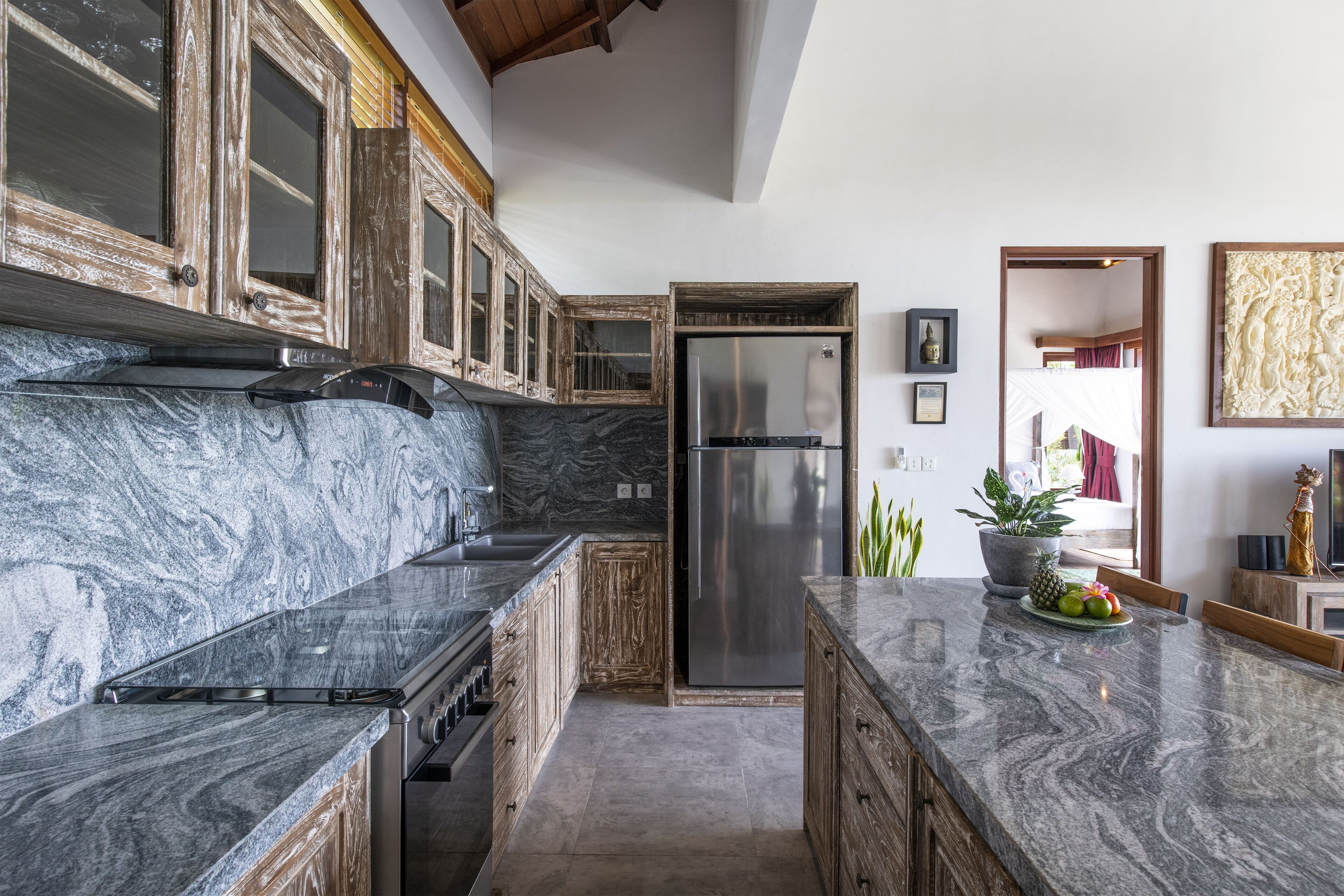 A kitchen with marble countertops, wooden cabinets, a stainless steel refrigerator, and a potted plant.