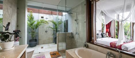 A modern bathroom with a glass-enclosed shower, a large bathtub, and a view of a bedroom with a canopy bed.