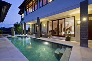 A modern poolside area with a clear pool, lounge chairs, and a well-lit interior space with a bed and curtains. - Sahaja Sawah Resort (Selemadeg)