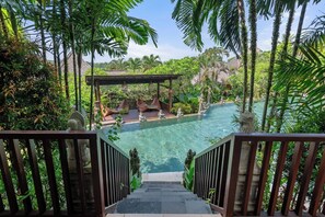 Un área de piscina con una escalera de piedra que baja hacia ella, rodeada de exuberante vegetación y palmeras.
