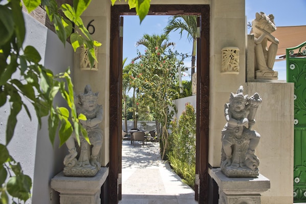 Un sendero que lleva a un patio con una estatua a la izquierda y una puerta verde a la derecha.