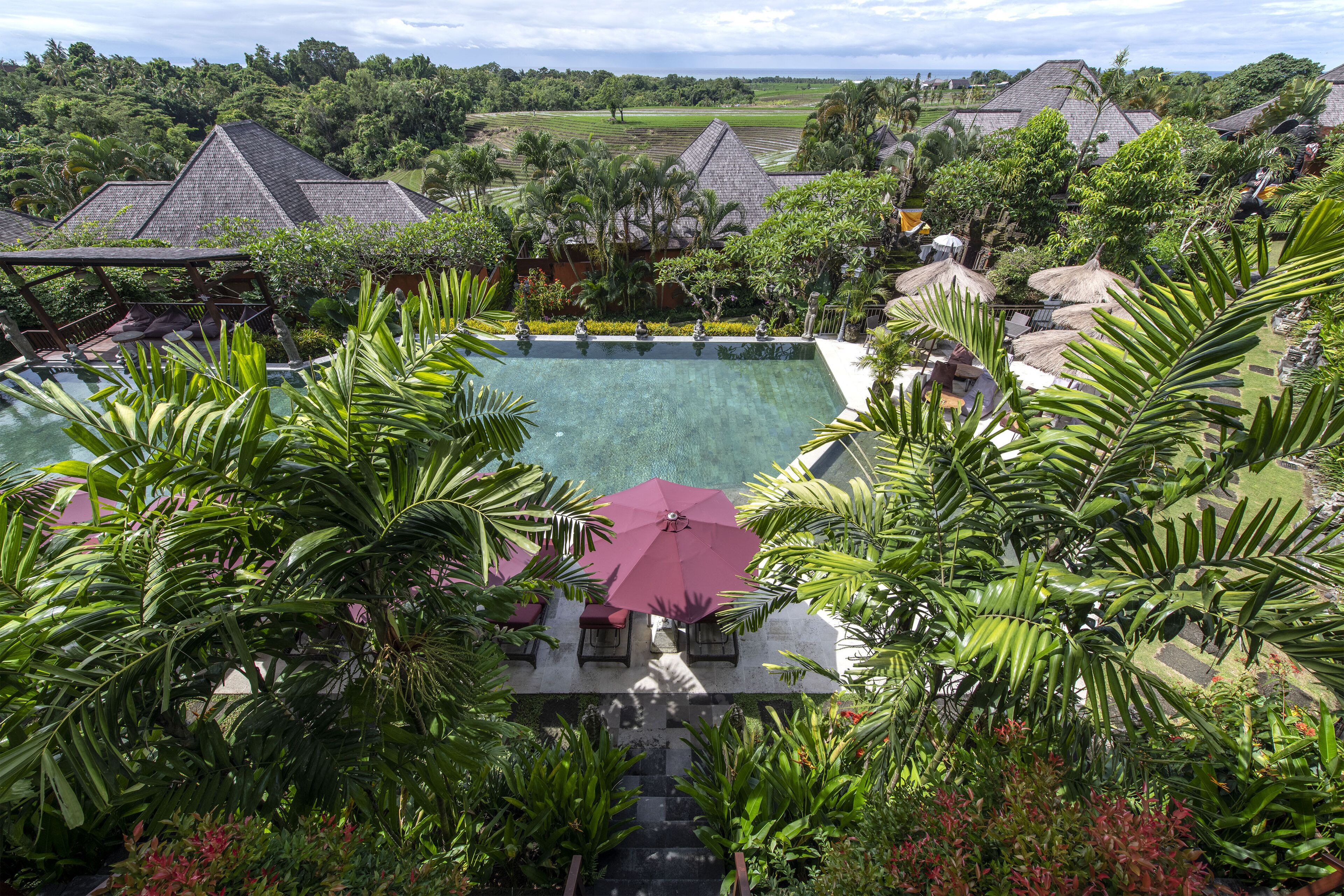 A resort with a large swimming pool surrounded by lush greenery and thatched-roof structures.
