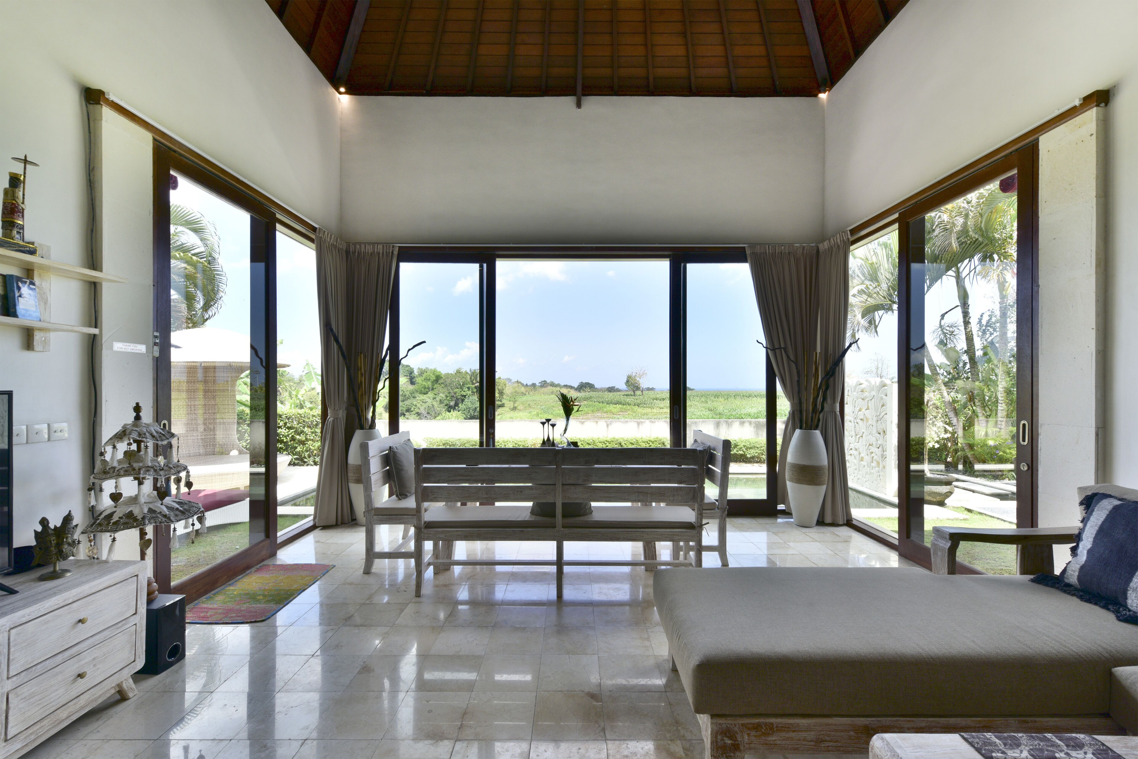 A spacious room with a large bed, a bench, and a dining table. There are large windows providing a view of the outdoors.