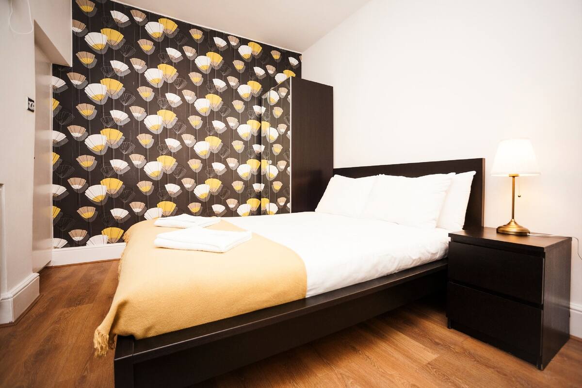 Ein modernes Hotelzimmer mit Bett, Nachttisch und einer Wand mit strukturierter Tapete.