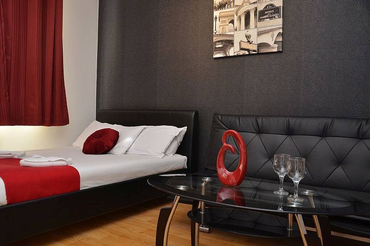 Ein Hotelzimmer mit einem Bett, einem Sofa, einem Glastisch mit zwei Weingläsern und einem roten Dekorationselement.