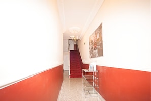 A hallway with red walls, a chandelier, a red carpeted staircase, and a metal rack with items on it. - Hyde Park Apartments (London)