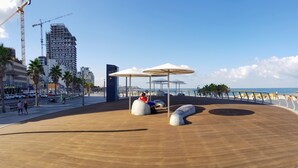 A wooden deck with modern seating and umbrellas, overlooking a beach and a cityscape with construction cranes. - Central Hotel (Tel Aviv)