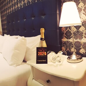 A hotel room with a tufted headboard, a bedside table with a champagne bottle, glasses, and a "2020 Happy New Year" card from Central Hotel. - Central Hotel (Tel Aviv)