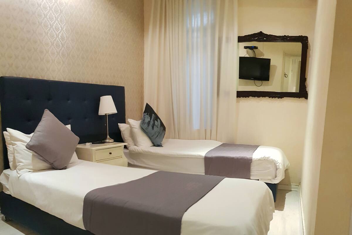 A hotel room with two beds, a nightstand, a lamp, a TV, and a mirror.