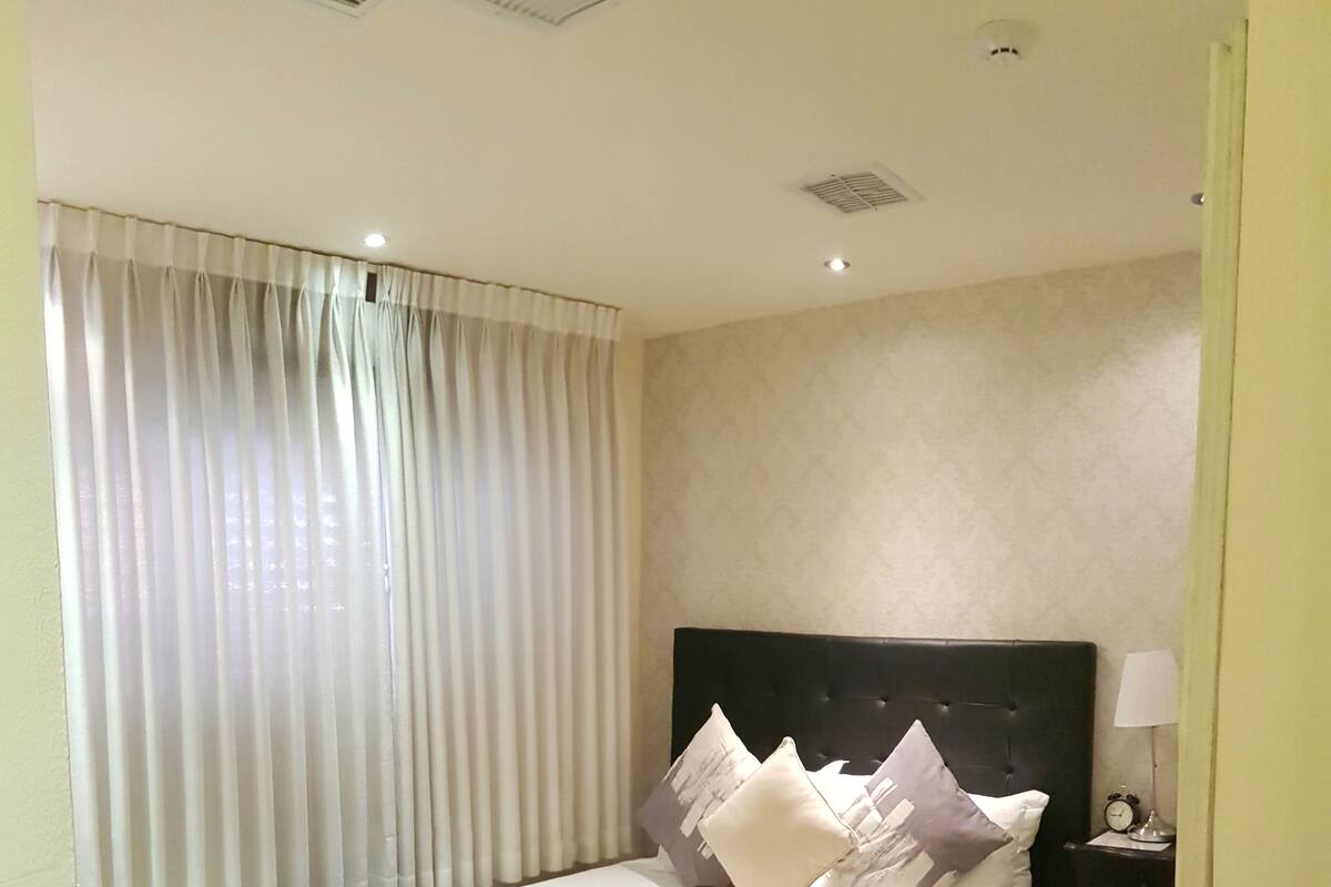 A hotel room with a large bed, a nightstand, a lamp, and a window with curtains.