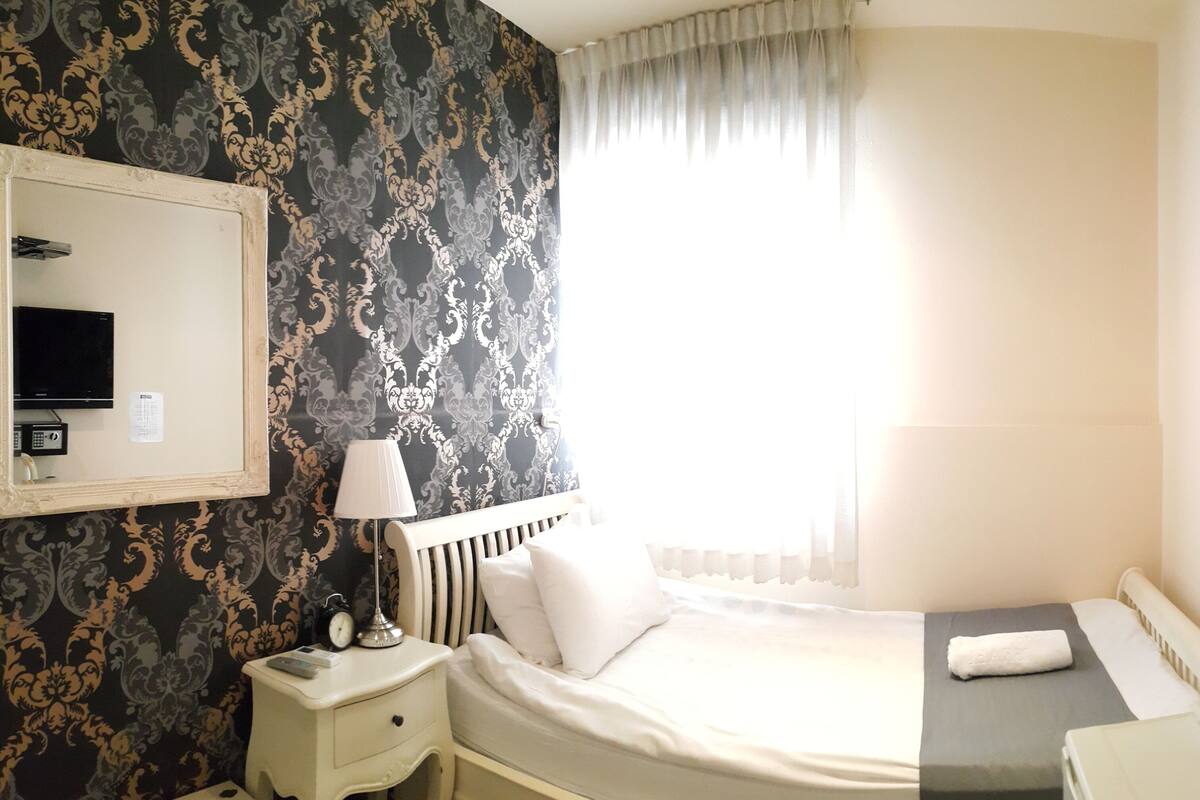 A hotel room with a bed, a nightstand, a lamp, a television, and a kettle.