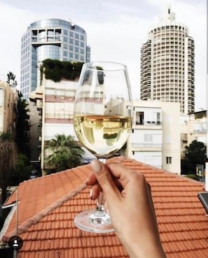 A hand holding a wine glass with a cityscape in the background. - Central Hotel (Tel Aviv)