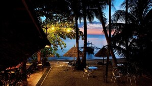 A beachside setting with thatched umbrellas, chairs, and a view of the ocean at dusk. - Easy Diving and Beach Resort (Sipalay)