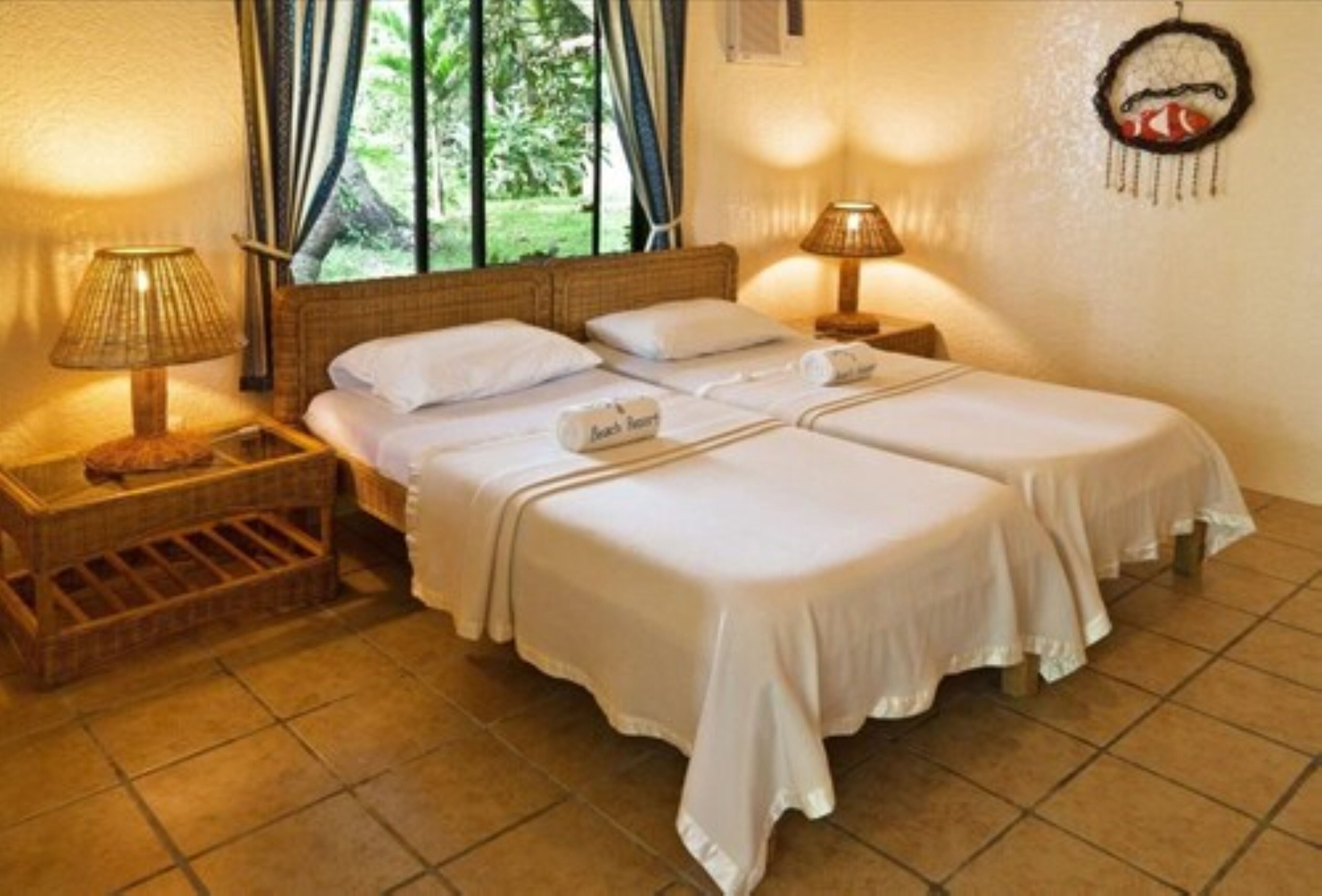 A double bed with white linens, two bedside tables with lamps, and a small wicker basket.