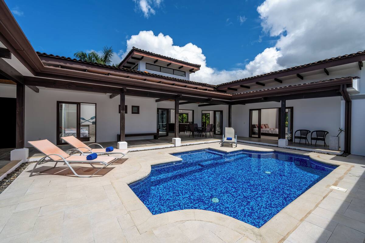 A modern house with a swimming pool, sun loungers, and a covered patio area.