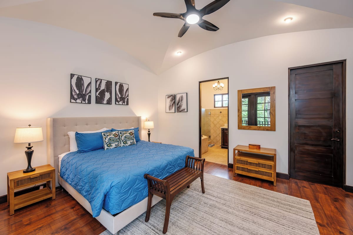 A bedroom with a large bed, a wooden bench, a nightstand, a mirror, and a door.