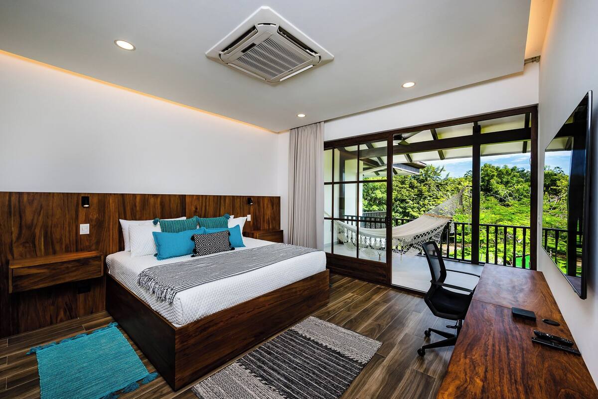 A modern bedroom with a large bed, wooden headboard, and a balcony with a hammock.