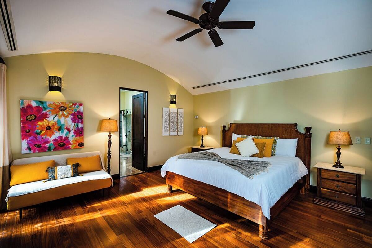 A bedroom with a wooden bed, a sofa, and a ceiling fan.