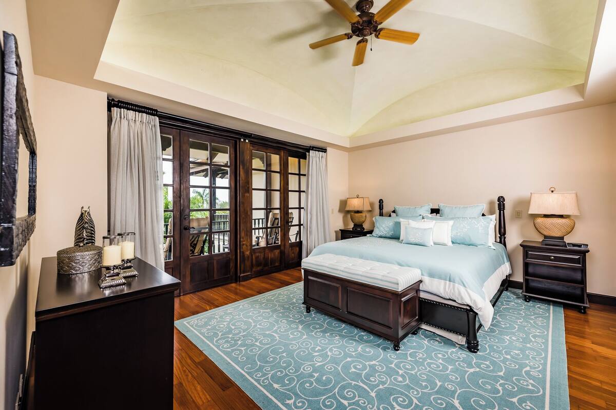 A bedroom with a bed, bedside tables, a desk, a ceiling fan, and a view through a glass door.