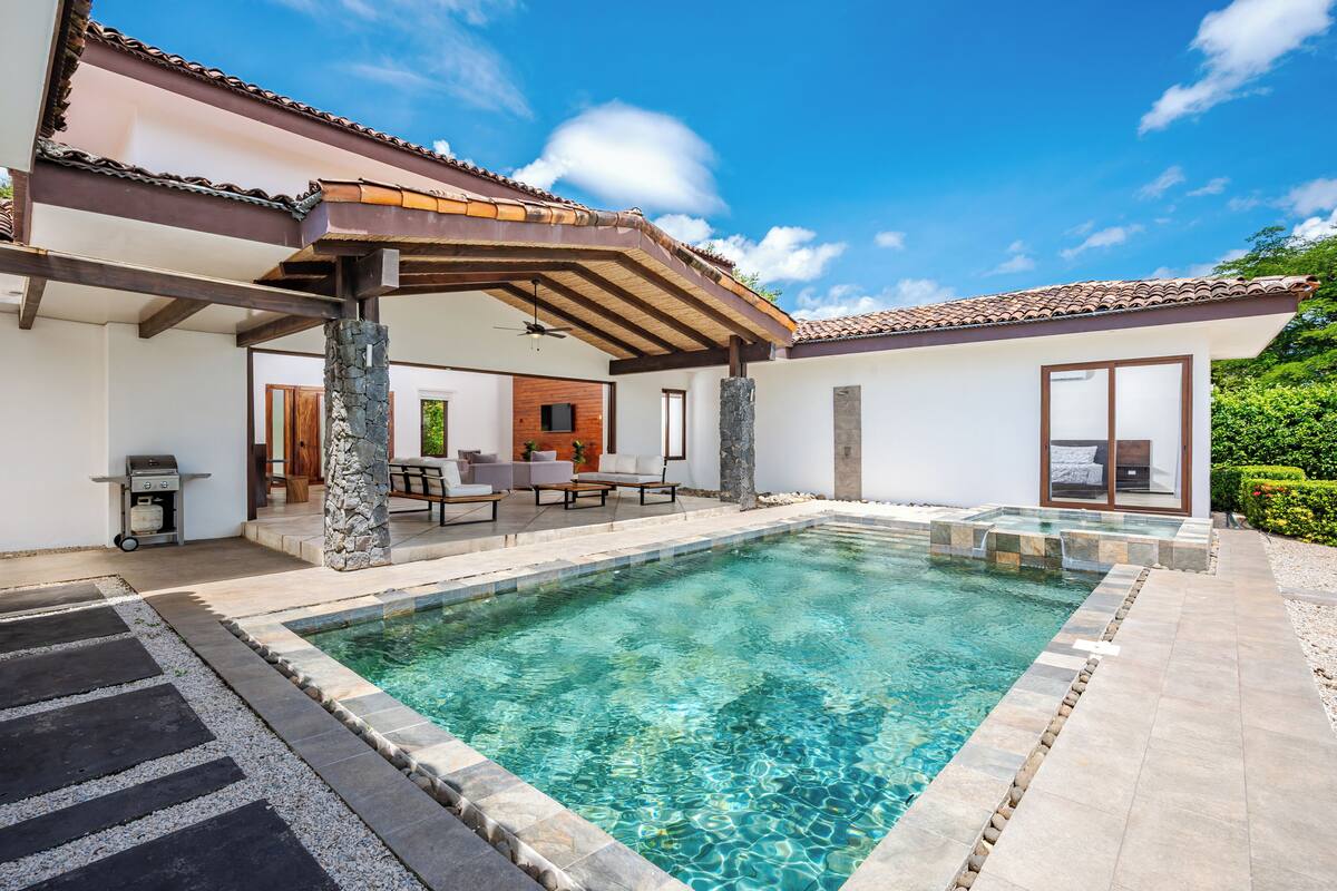 A swimming pool with a stone deck, outdoor seating, and a covered patio area.