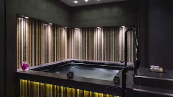 Een moderne spa met een verwarmde vloer, een groot bad en een decoratieve wand met verticale strepen.