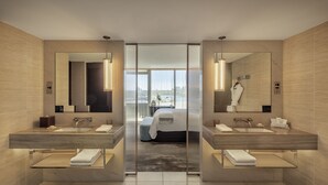 Un baño de hotel moderno con lavamanos dobles, espejos grandes y vistas de la ciudad a través de ventanales de piso a techo.