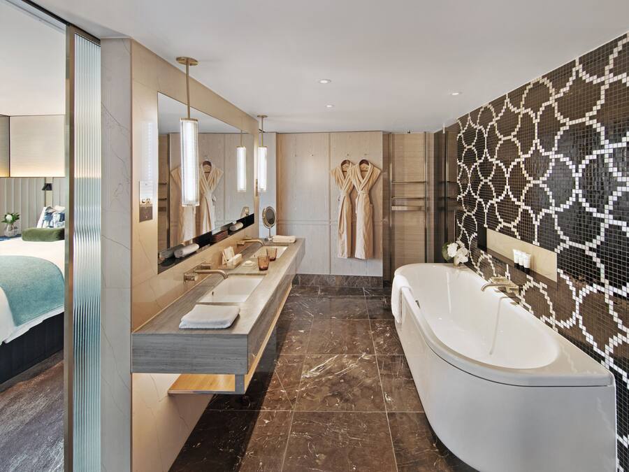 A modern bathroom with a large bathtub, a double vanity with a mirror, and a patterned wall.