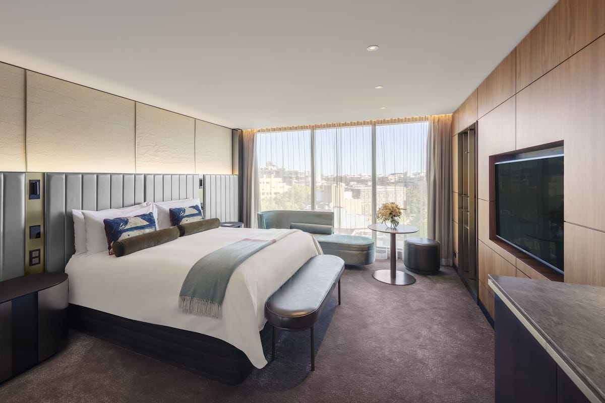 Una habitación de hotel moderna con una cama grande, televisor, zona de estar y vistas a la ciudad.