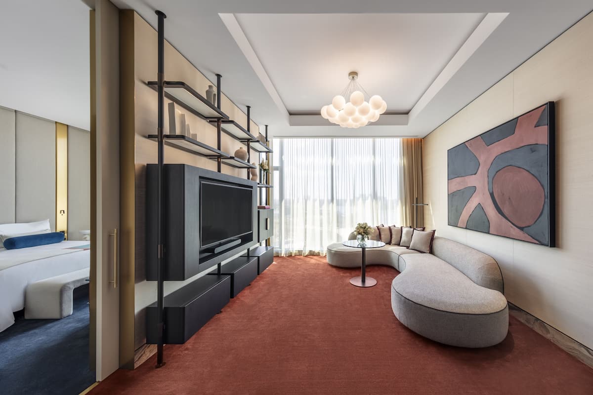 Una habitación de hotel moderna con un televisor de pantalla plana, un sofá, una mesita de centro y un cuadro abstracto grande en la pared.
