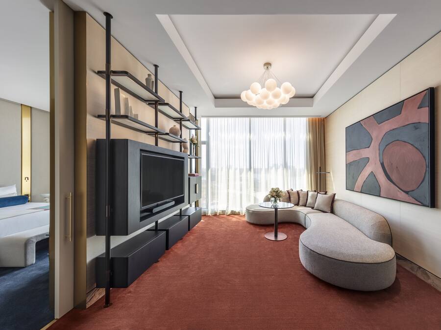 A modern hotel room with a flat-screen TV, a sofa, a coffee table, and a large abstract painting on the wall.