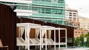 Una piscina con tumbonas blancas y un edificio moderno al fondo.