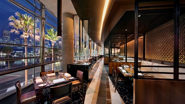 Un restaurante moderno con vistas al horizonte de la ciudad, que cuenta con techos altos, ventanas amplias y una pared con diseño.