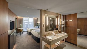 Una habitación de hotel moderna con una cama grande, una zona de escritorio separada, un espejo amplio y un lavamanos doble.