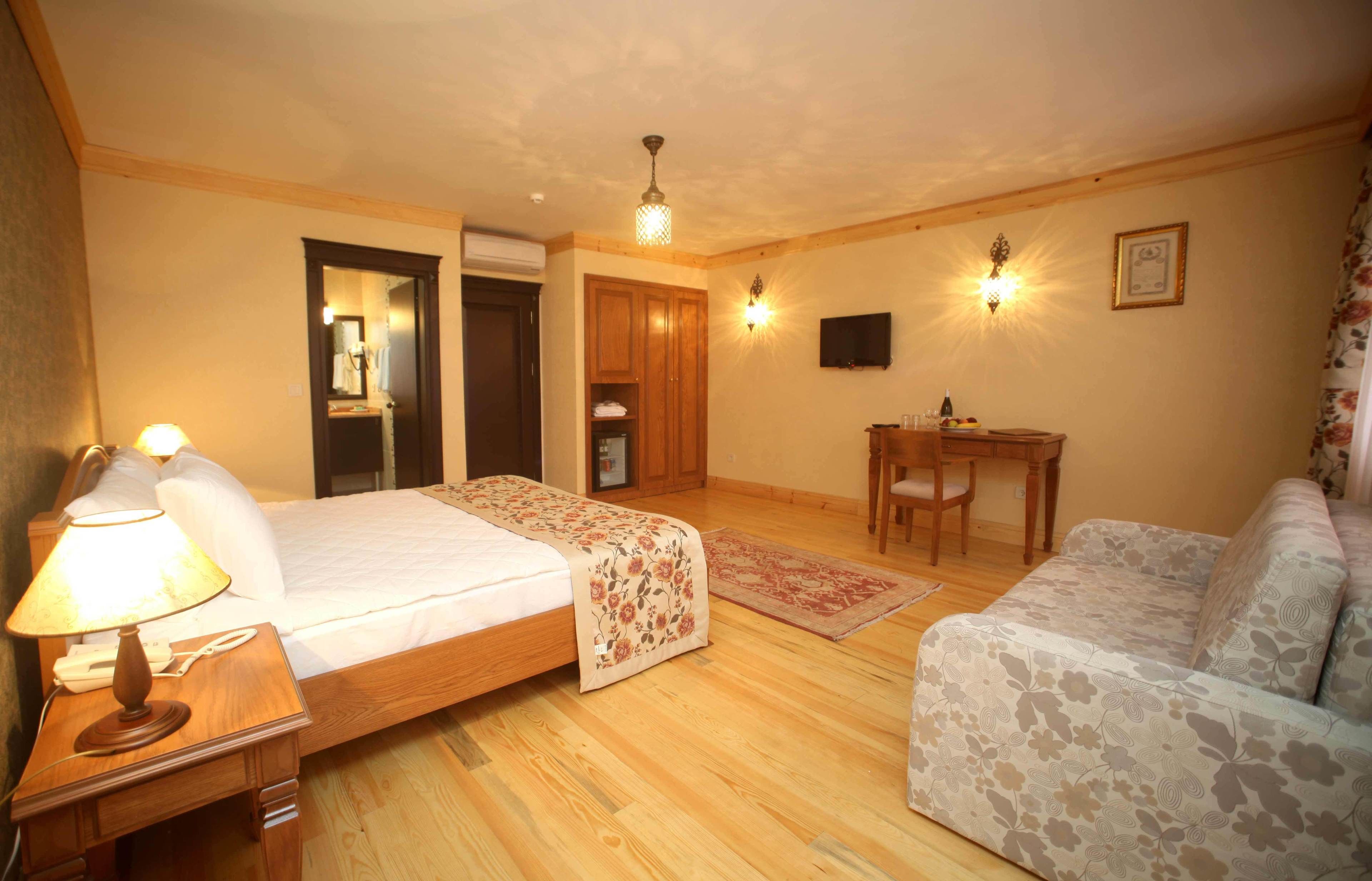 A bedroom with a bed, a desk, a chair, a sofa, and a lamp.