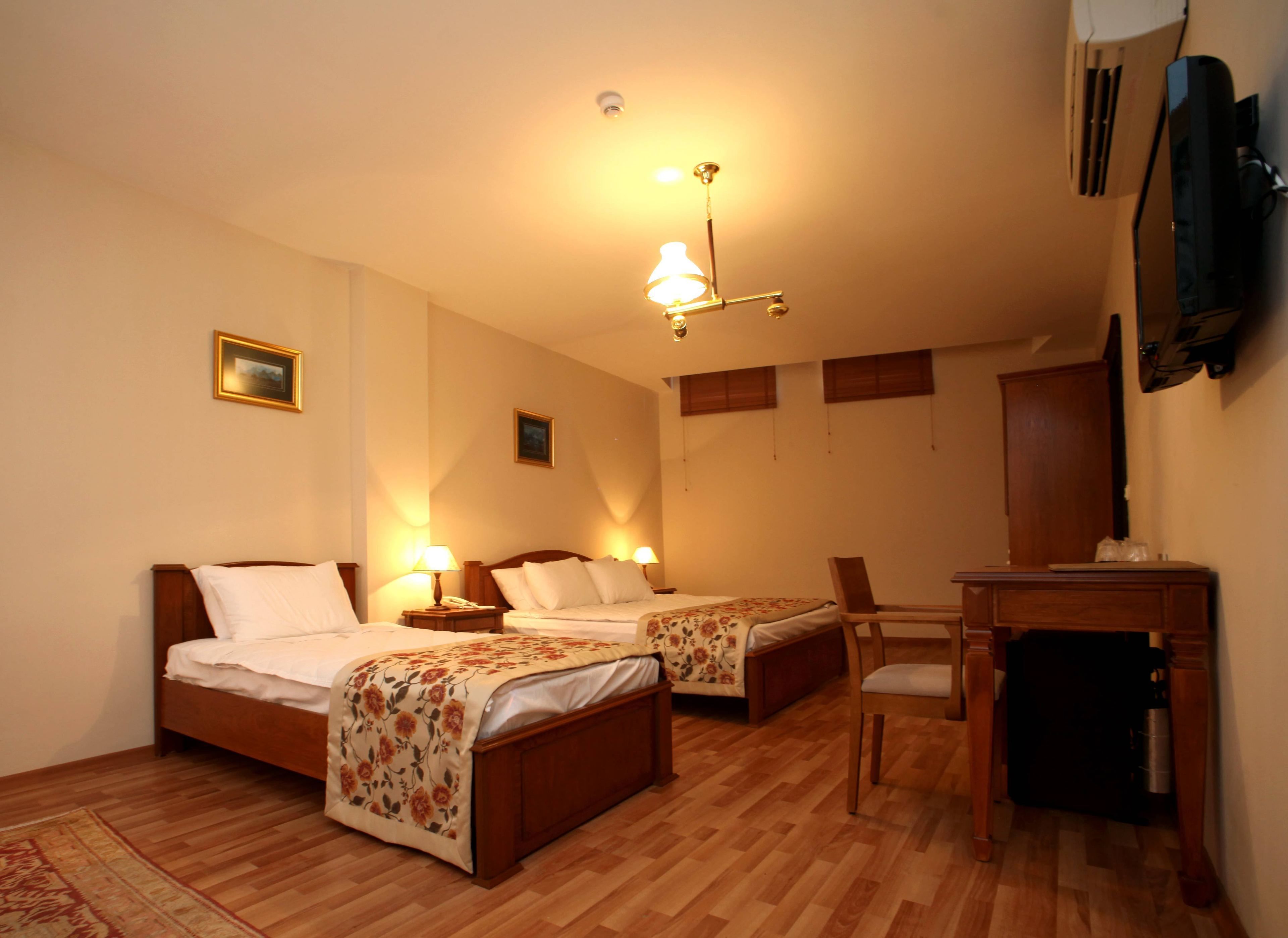 Habitación de hotel con dos camas individuales, un escritorio de madera, una silla y un televisor en la pared.