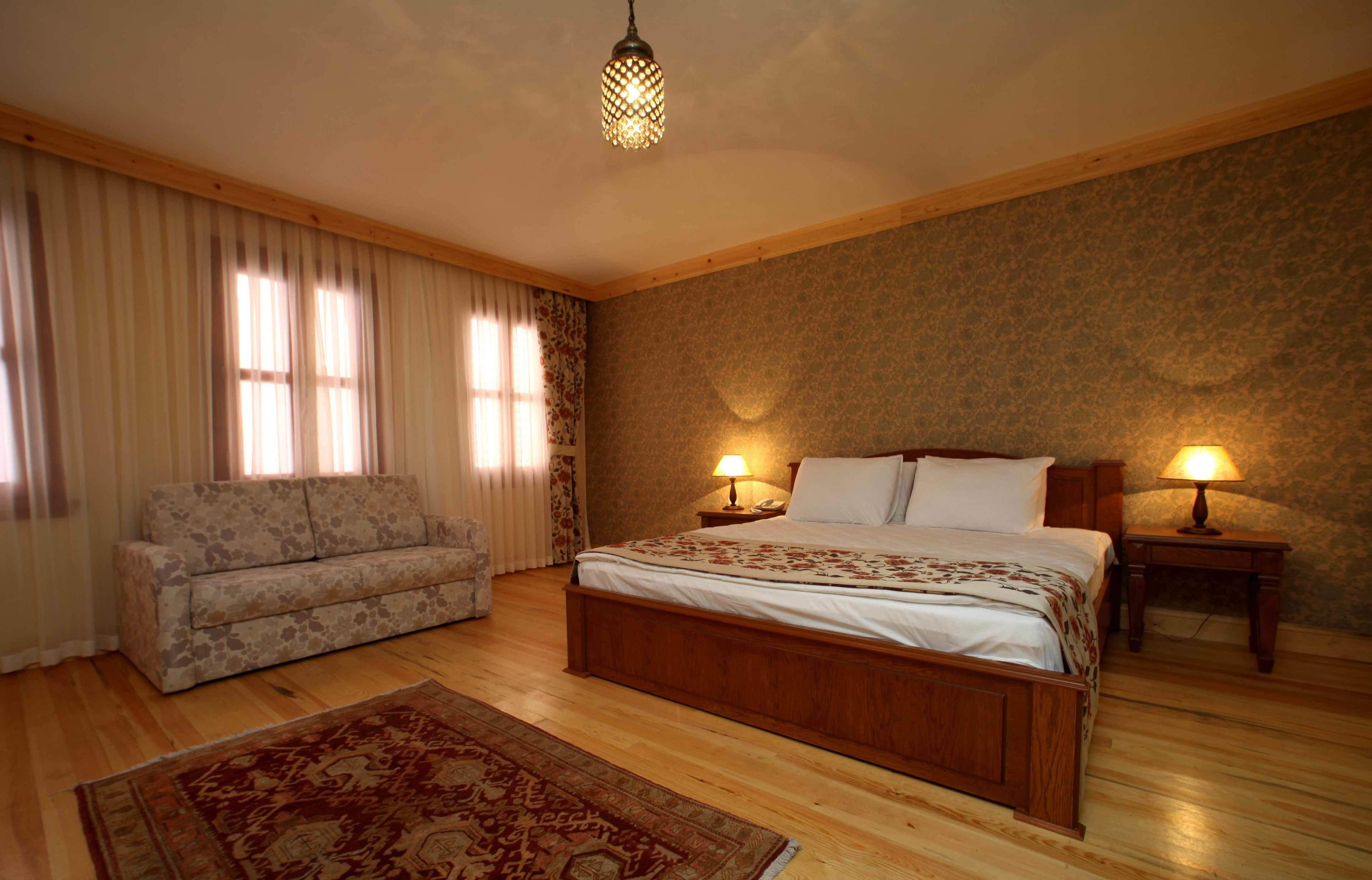 Un dormitorio con una cama de madera, dos lámparas de noche, un sofá y una alfombra estampada.