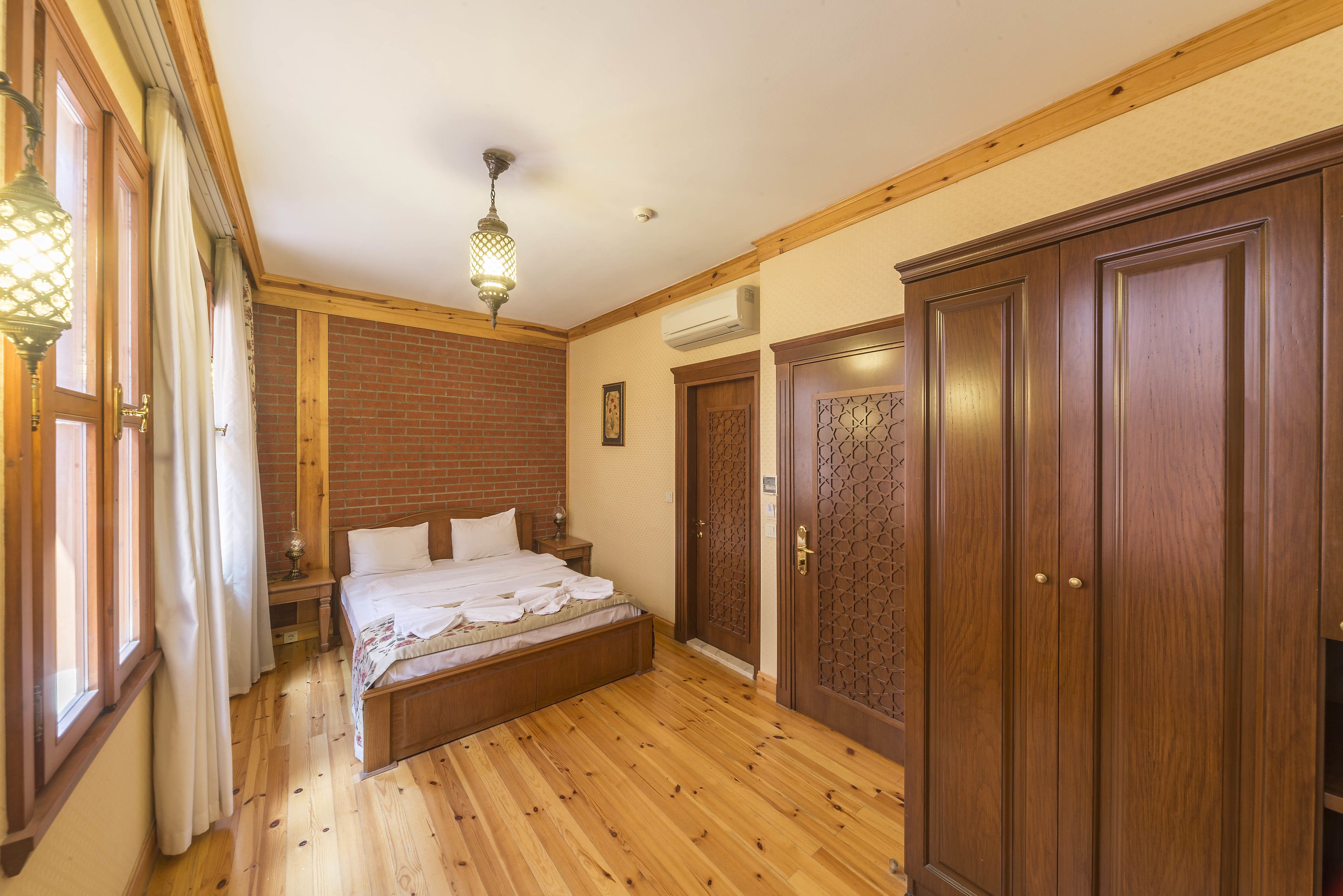 Een slaapkamer met een houten vloer, een bed, een nachtkastje, een lamp en een kledingkast.