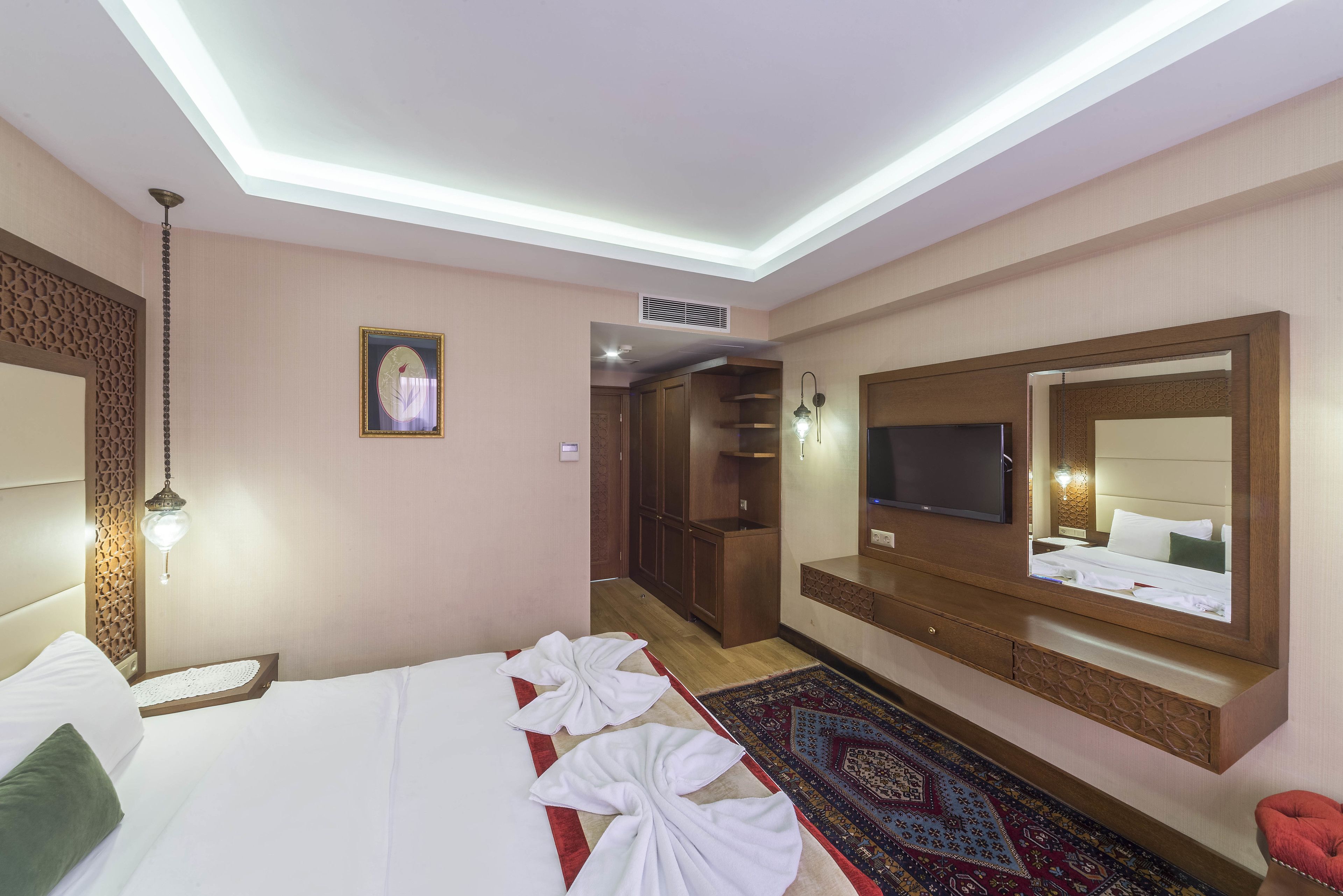 Una habitación de hotel con cama, televisor, espejo, armario y alfombra.