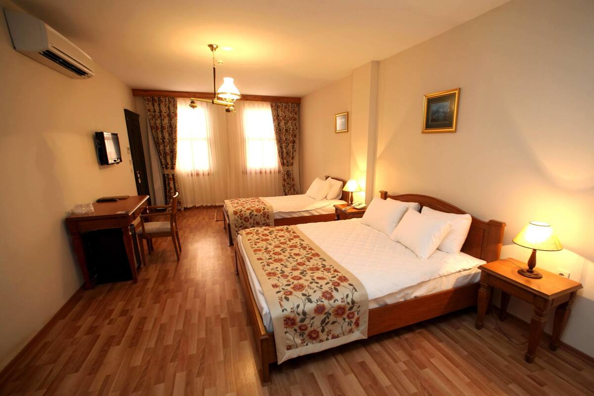 A hotel room with two beds, a desk, a chair, and a lamp.