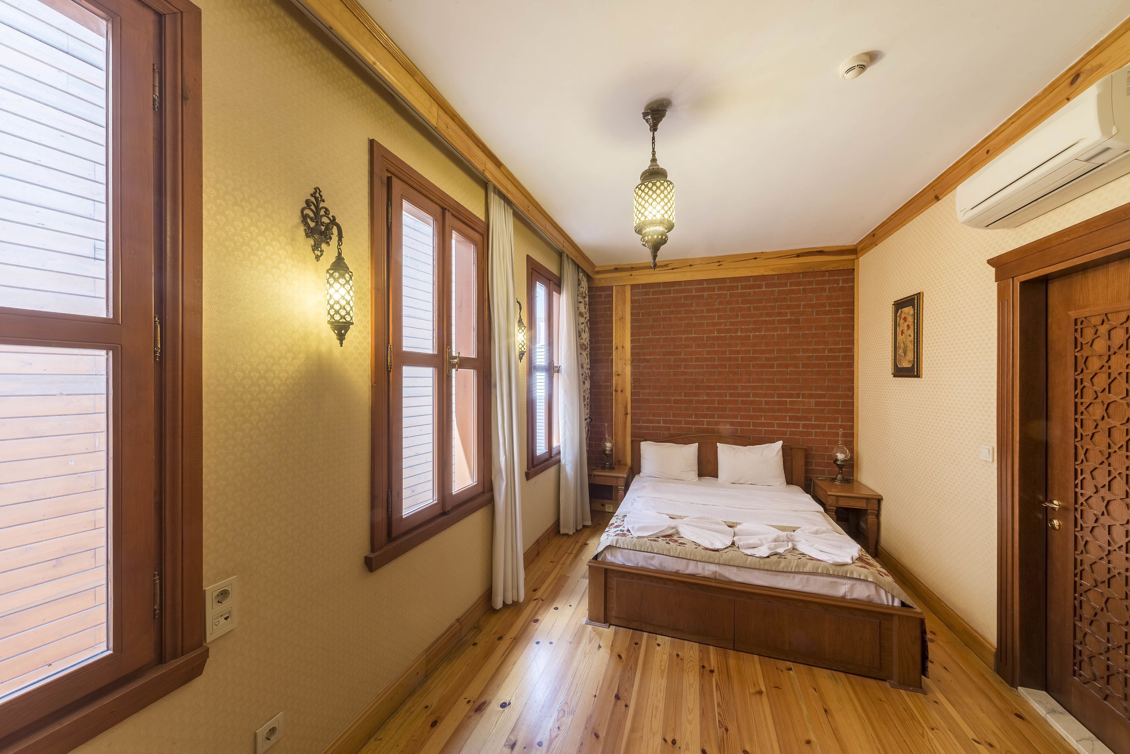 A bedroom with a wooden bed, a nightstand, a wall-mounted lamp, and a window with curtains.