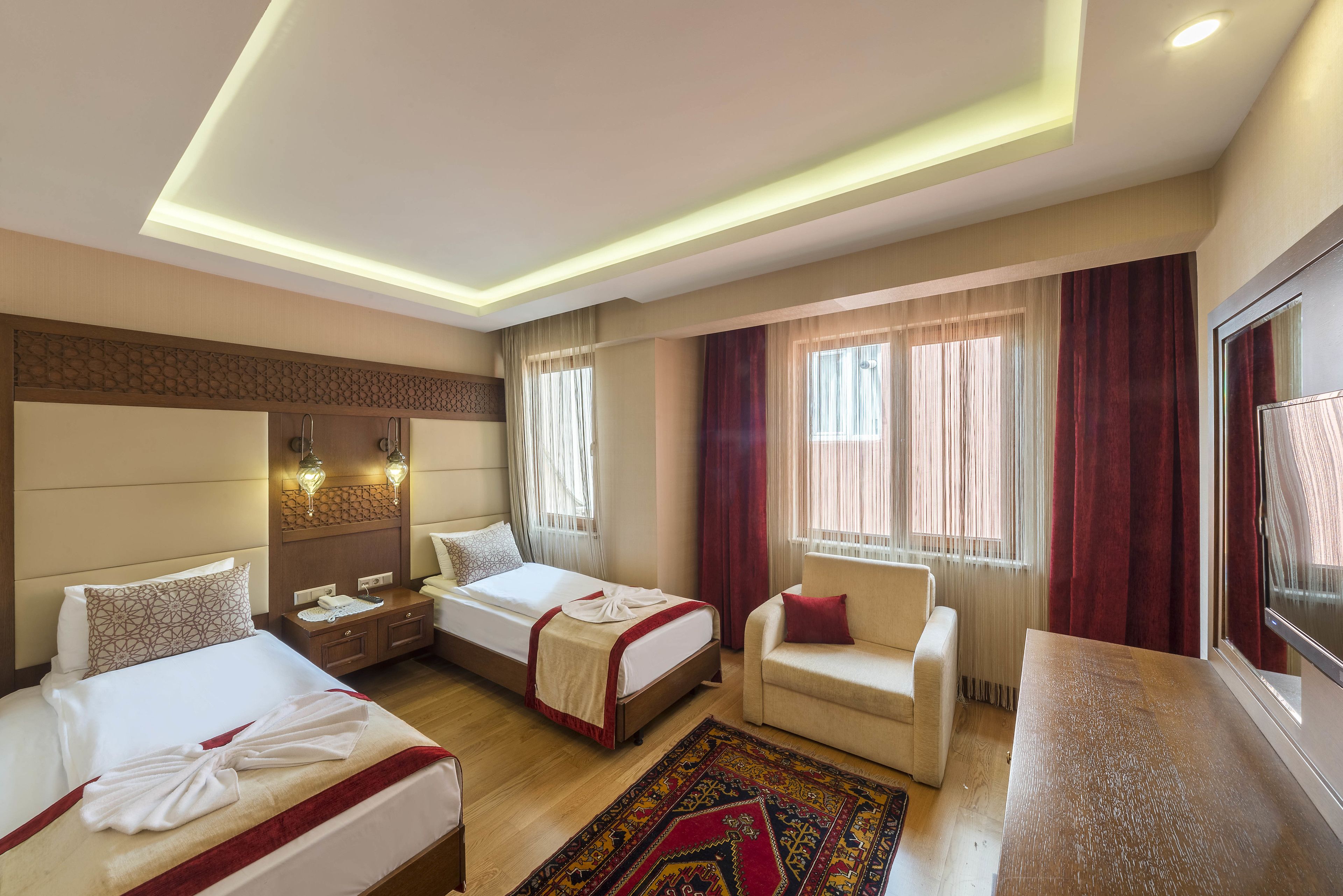 A hotel room with two beds, a sofa, a desk, and a large window with curtains.