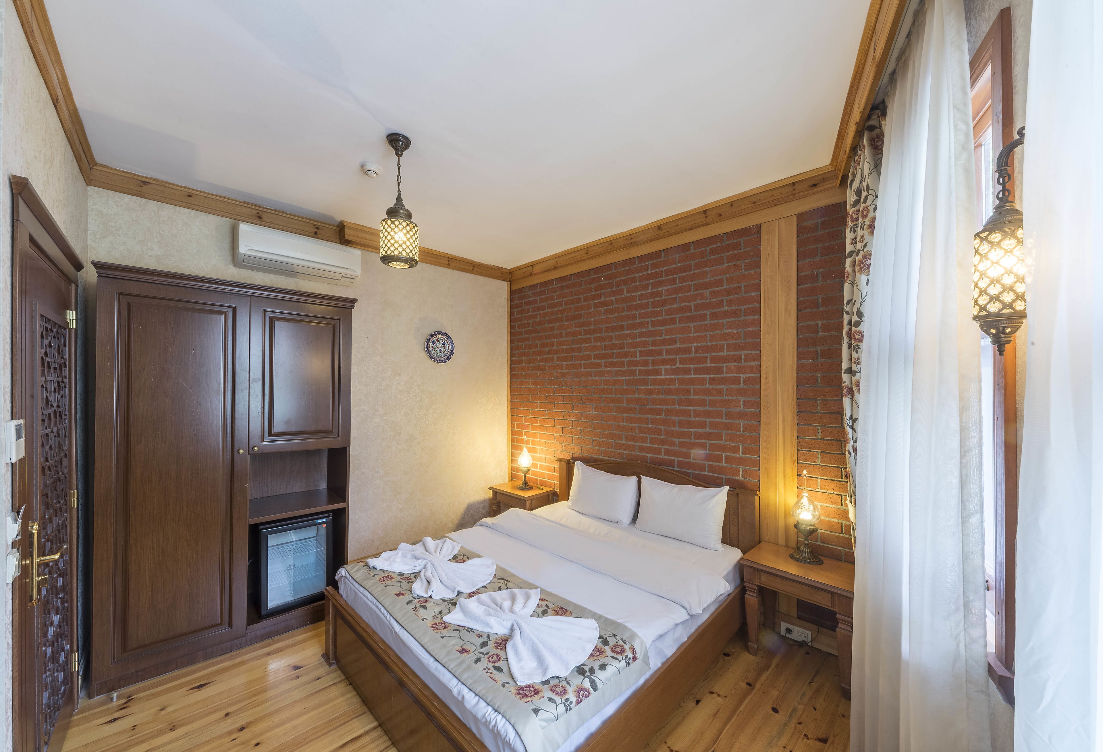 Quarto com cama de madeira, uma pequena mesa de cabeceira, um criado-mudo e um guarda-roupa embutido, com parede de tijolos.