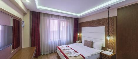 A hotel room with a bed, bedside table, TV, curtains, and a ceiling light.