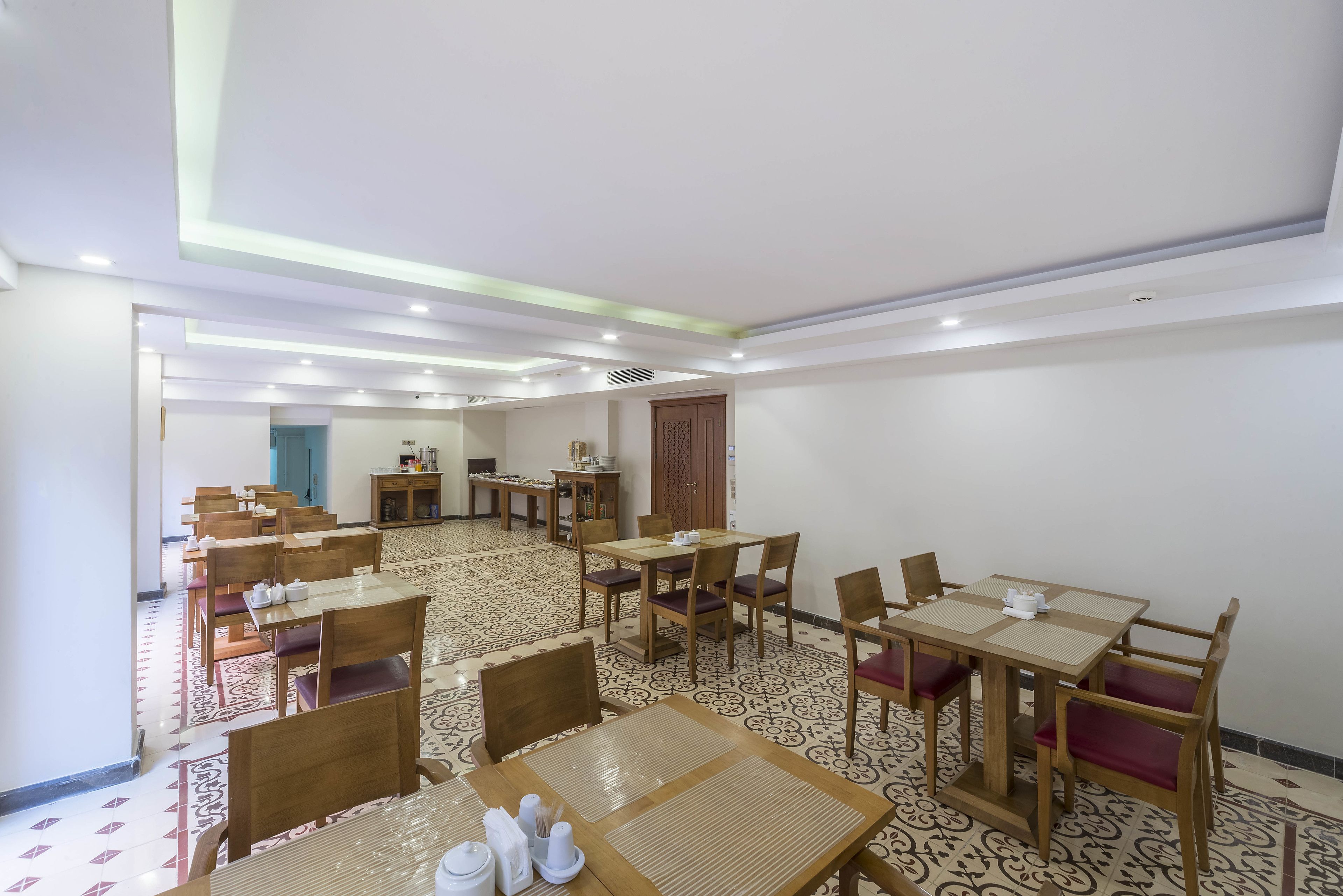 A hotel dining area with multiple tables and chairs, a patterned floor, and a ceiling with recessed lighting.