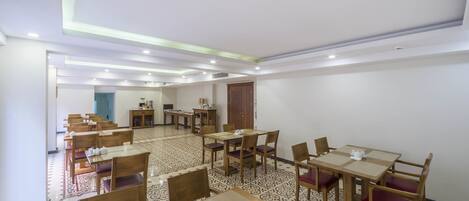 A hotel dining area with multiple tables and chairs, a patterned floor, and a ceiling with recessed lighting.