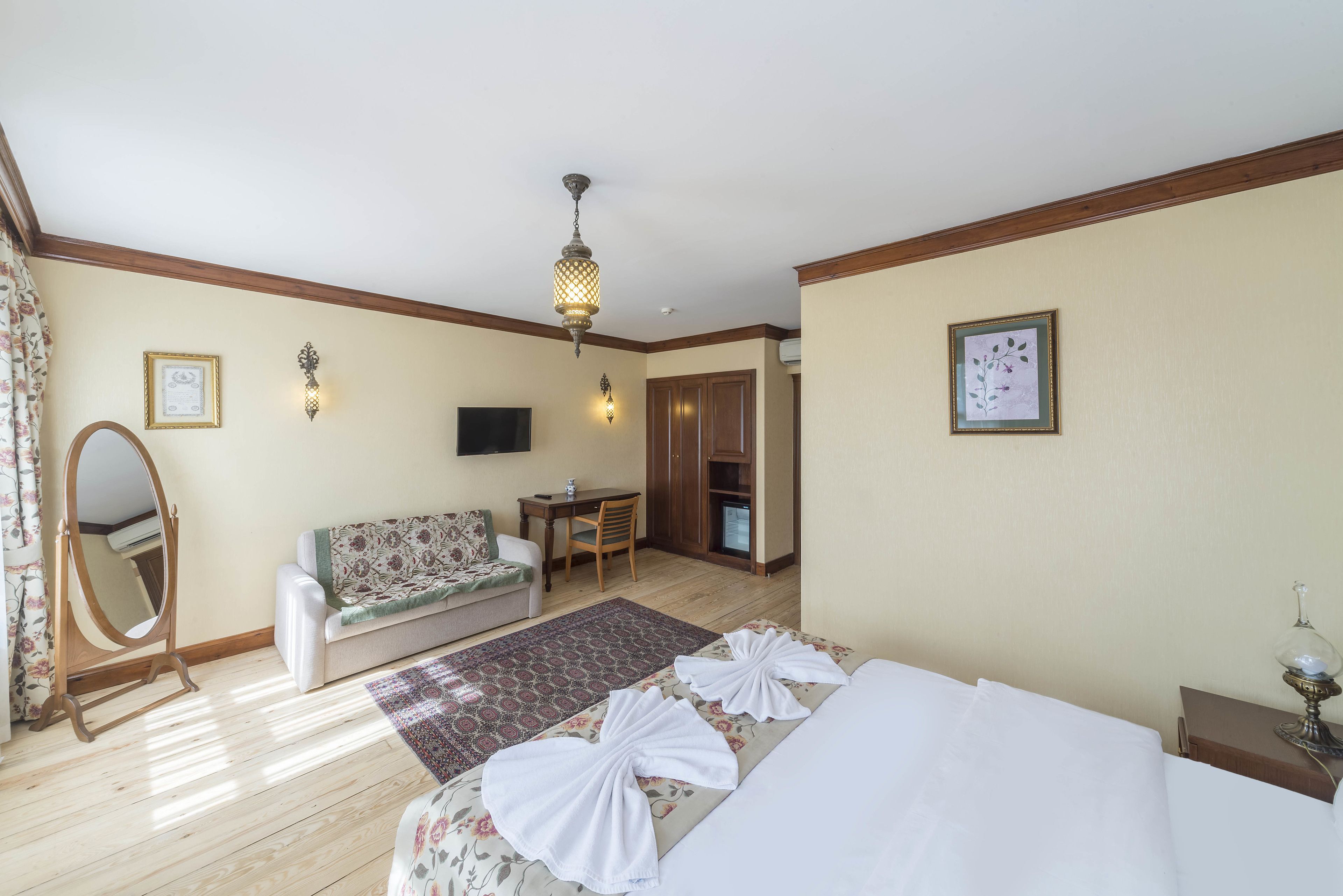 A hotel room with a bed, a sofa, a desk, a mirror, and a television.
